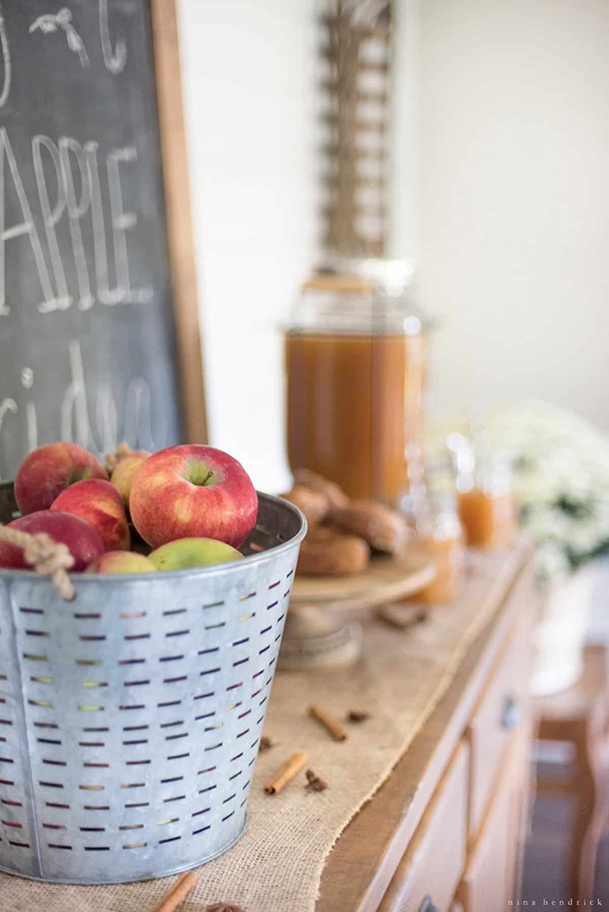 A galvanized bucket of apples on a table with desserts in the background.