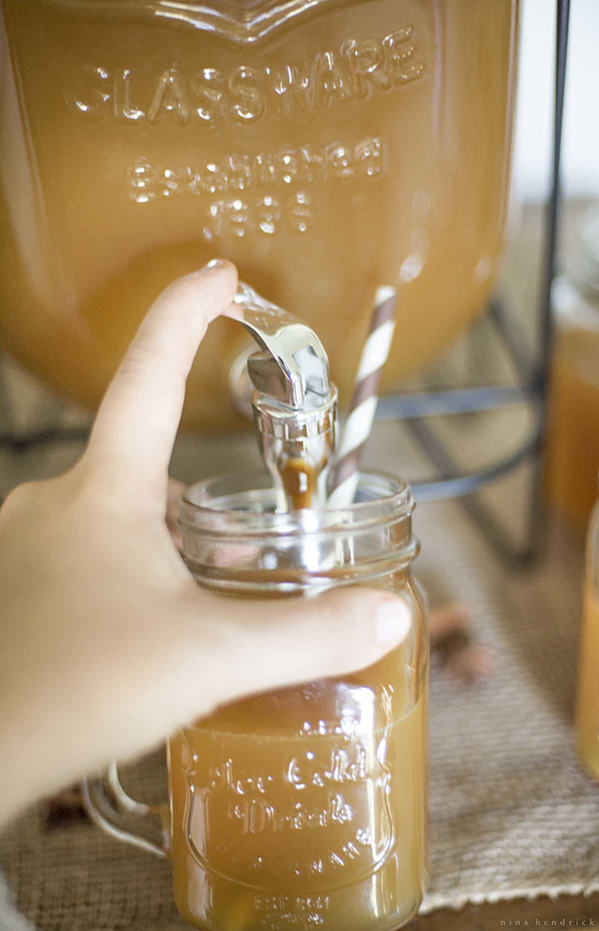 A person pouring apple cider into a mason jar from a beverage dispenser.