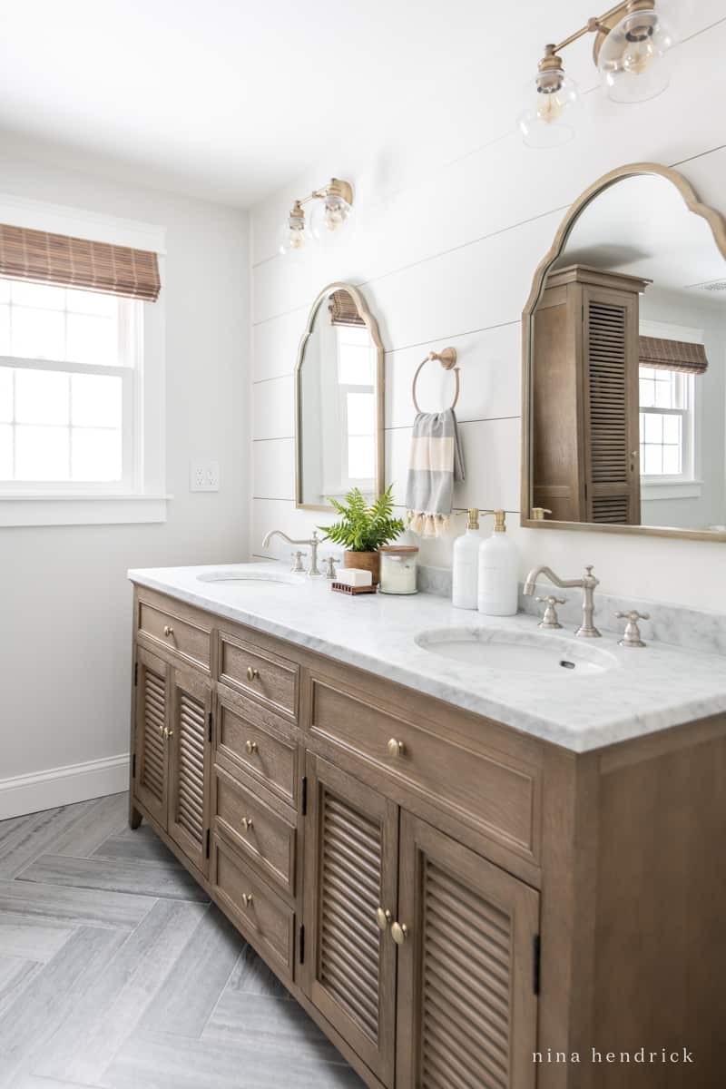 Cottage bathroom design ideas like shiplap walls and warm wood vanity with curved metal mirror