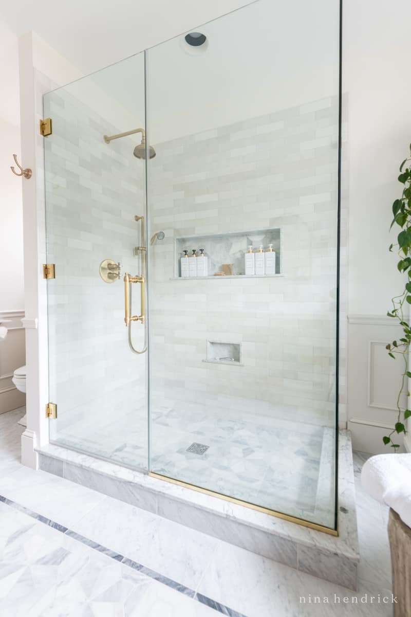 Glass shower enclosure with marble bathroom design and brass accents