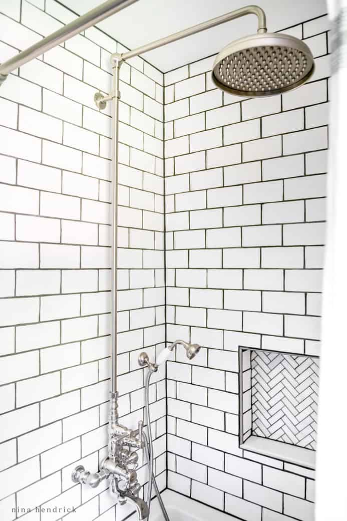 White subway tile with dark grout in an exposed-pipe shower tub.