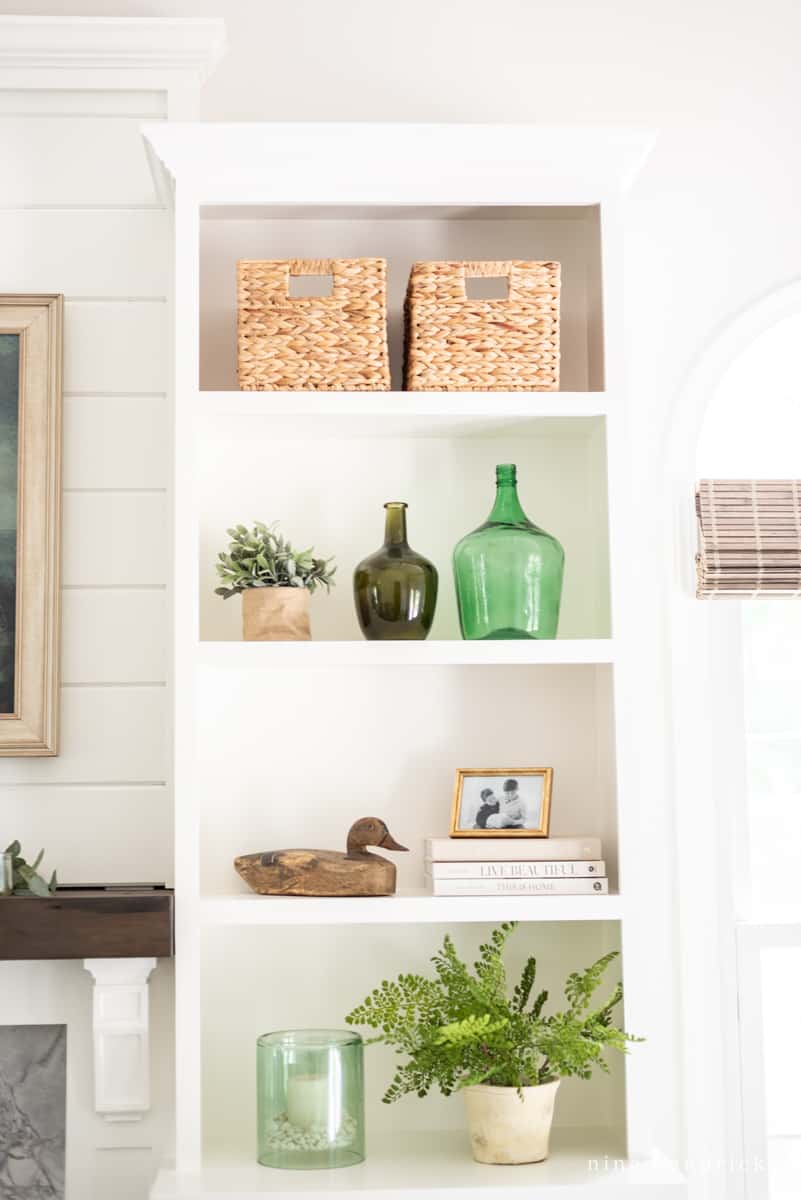 White built-in bookshelf beside the fireplace with plants, baskets, vases and other small decor items