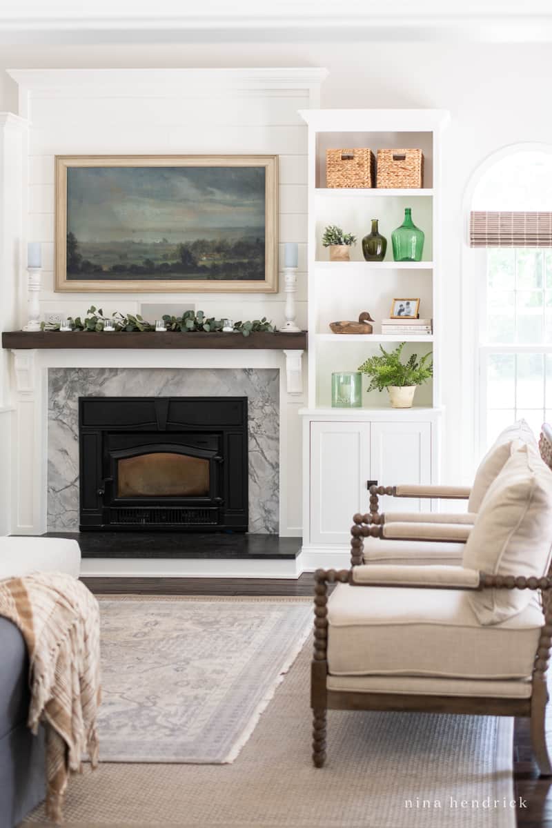 Living room with marble fireplace and Frame TV with built-in bookshelf filled with neutral decor