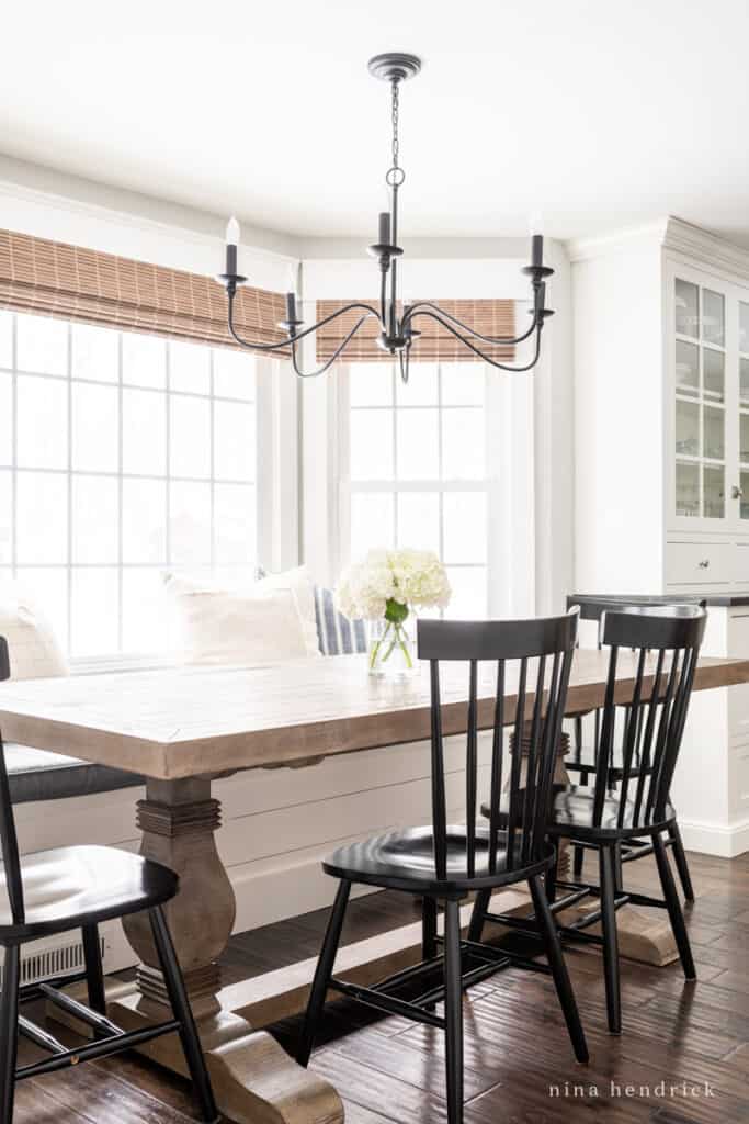 Dining area with bench and black Windsor chairs with iron chandelier and wood table