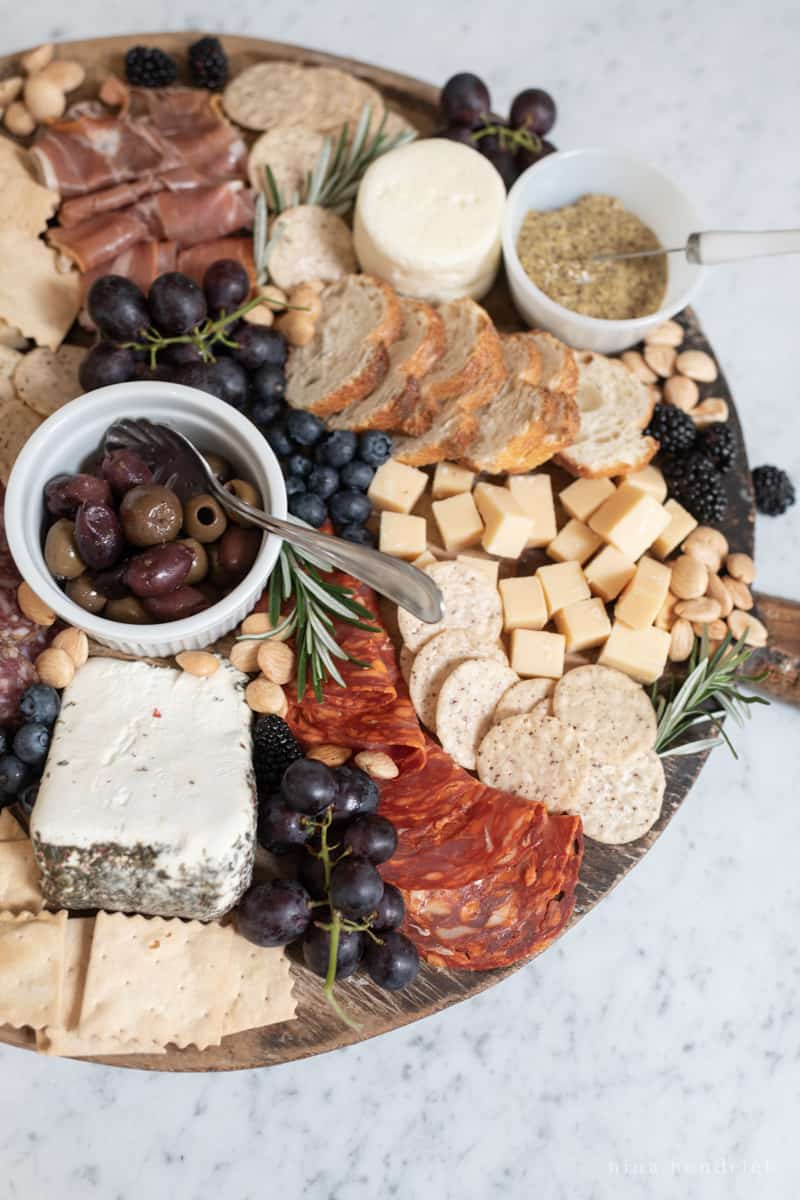 Overhead view of a cheese board with various meats, crackers, fruits, nuts, and olives.