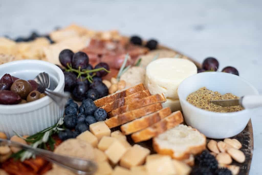 Close up shot of bread, mustard, and olives along with fruit 