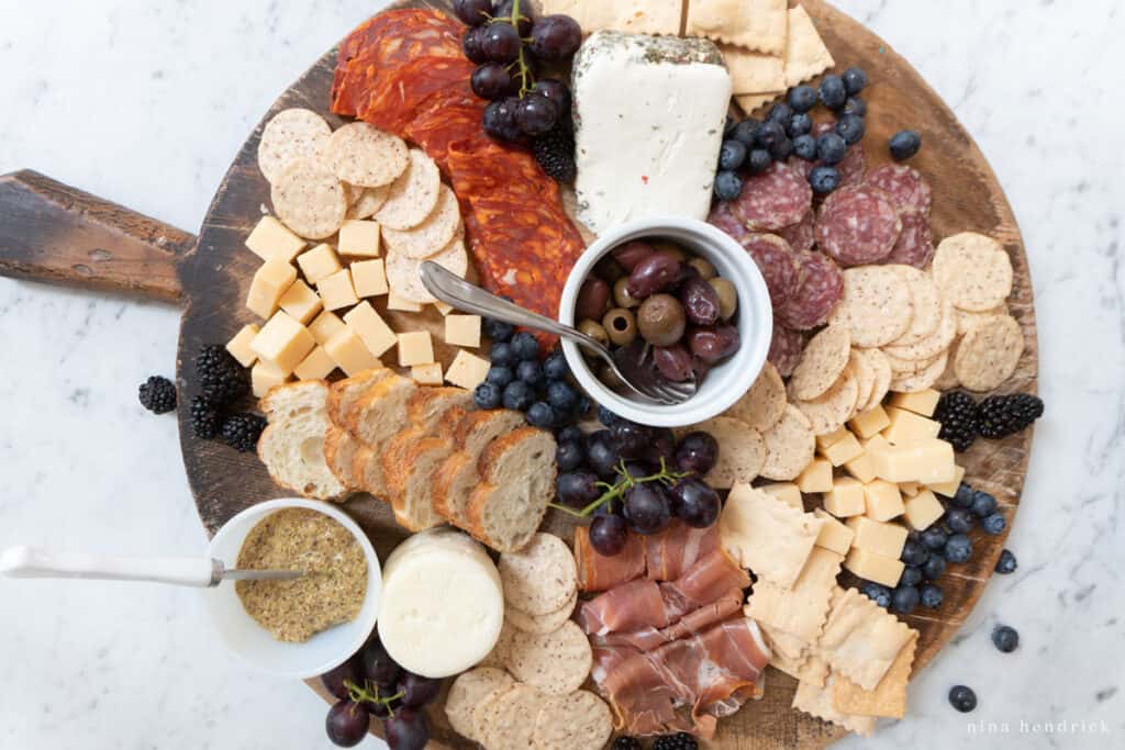 Step five for how to make a charcuterie board — add fruit like blueberries, grapes, and blackberries