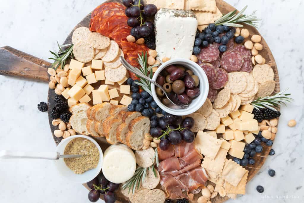 Charcuterie board with cheese, crackers, blueberries, salami, rosemary, and mustard