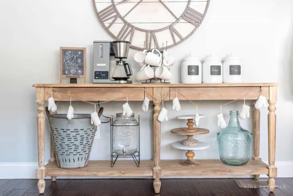 Create a coffee bar for your Christmas Brunch. Console table with mitten felt garland, coffee machine, mugs, and white jars