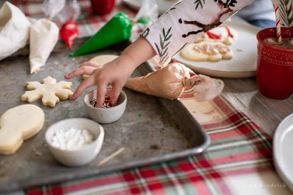 Child's hands reaching for sprinkles with cookies and icing in background