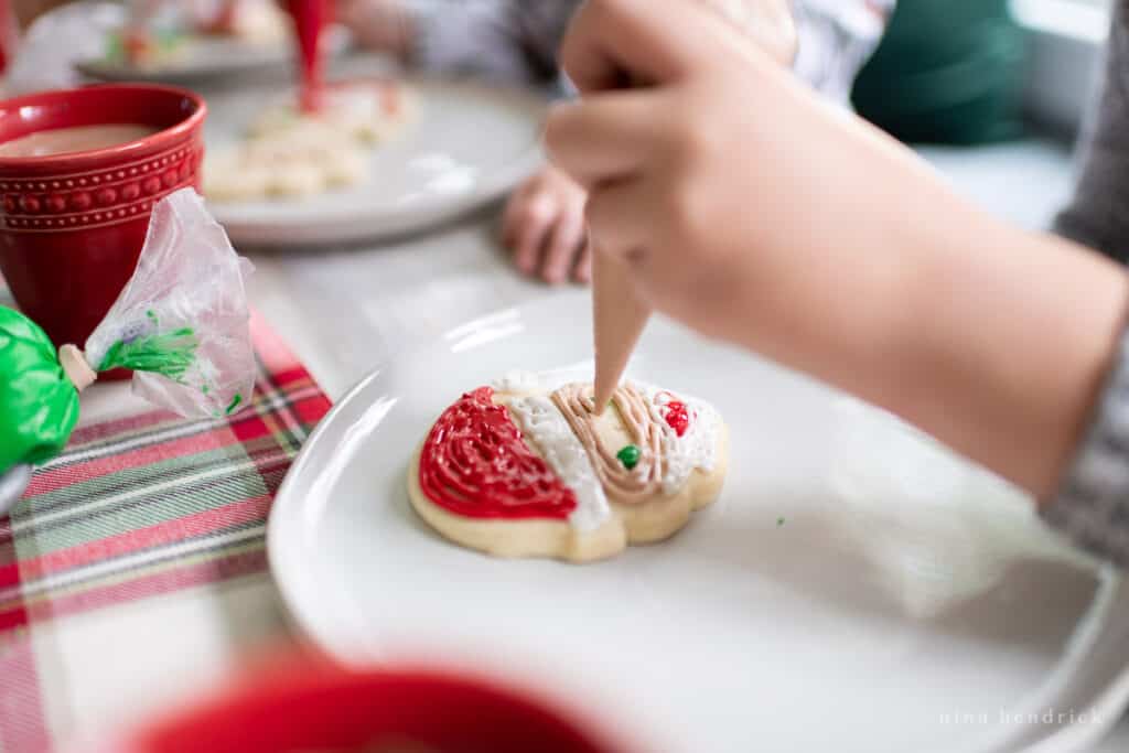 Santa Claus cookie being decorated by a child with hot chocolate in the background