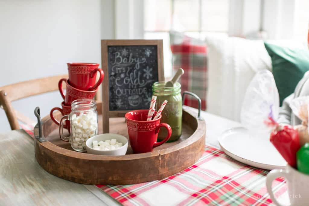 Red mugs, hot chocolate, a chalkboard, and marshmallows on a round wooden tray