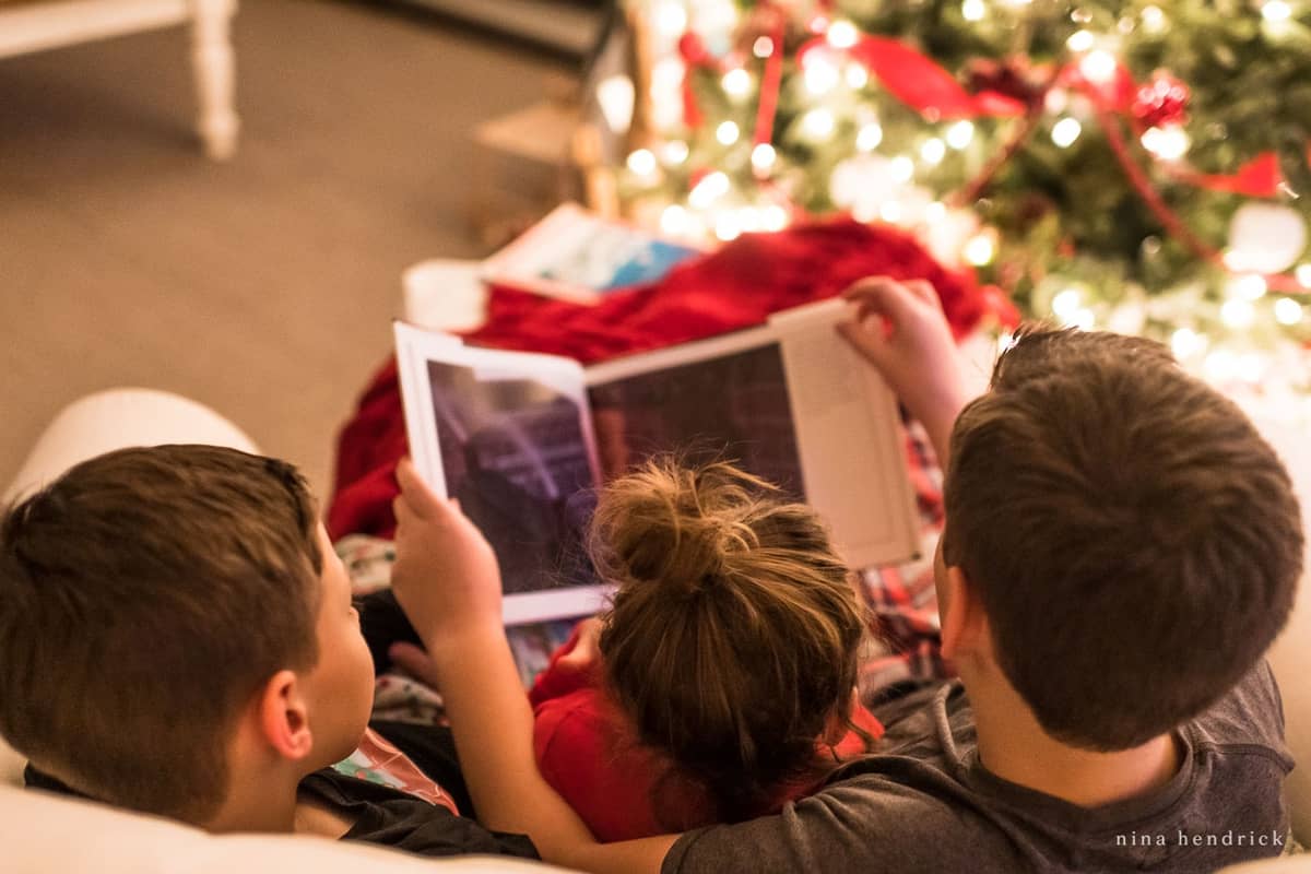 Children reading book with Christmas tree in background