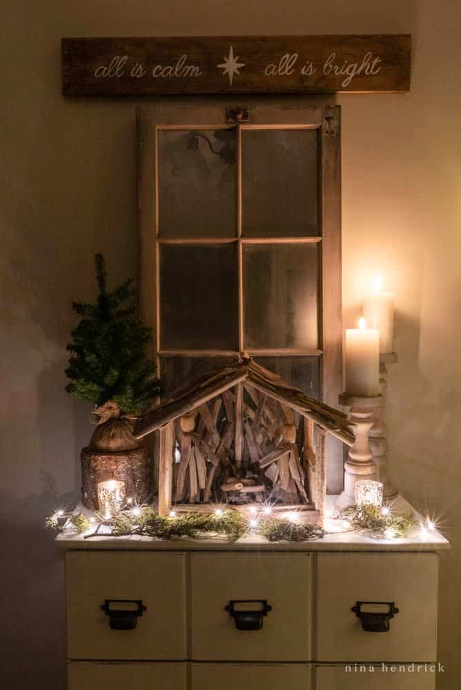 Christmas lights and Candles at night in the foyer with a nativity scene and a sign that says "All is Calm, All is bright"