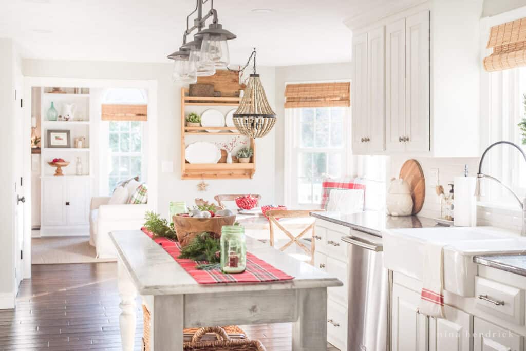 A kitchen with classic Christmas decorations including a wooden bowl with ornaments and a red plaid runner