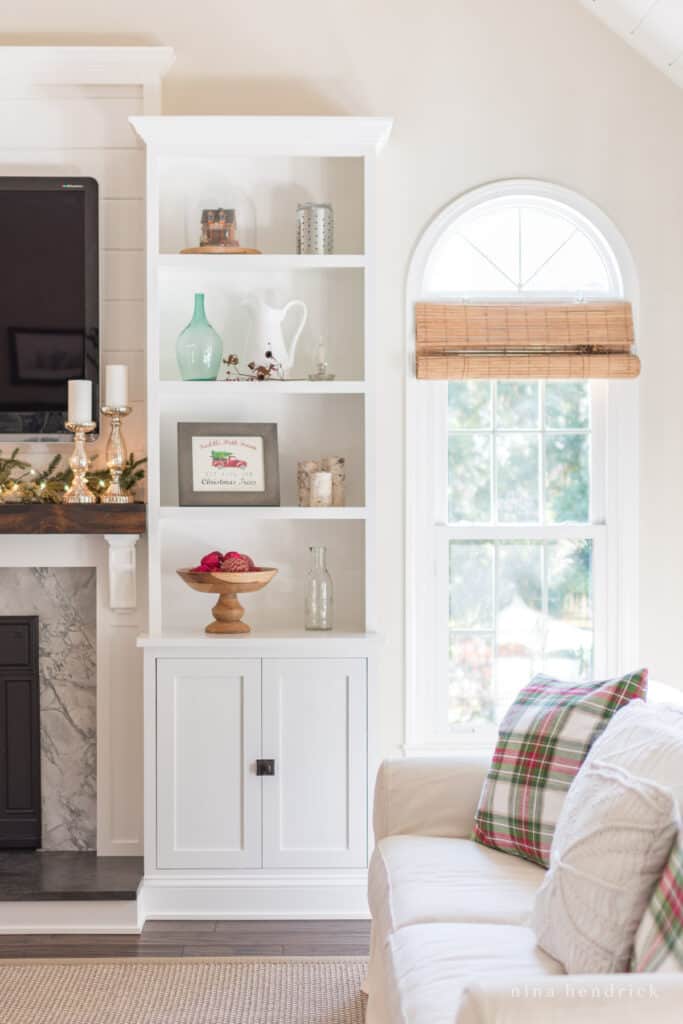 Sofa with red and green plaid pillows and a built-in bookcase with a Christmas Sign