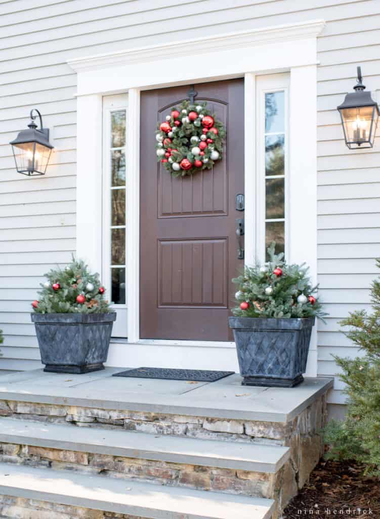 Front porch with planters filled with evergreens and ornaments and a holiday wreath on the wooden front door