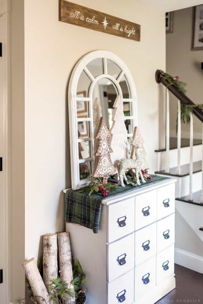 Foyer with white card catalog adorned with a Christmas vignette and an arrangement of birch logs