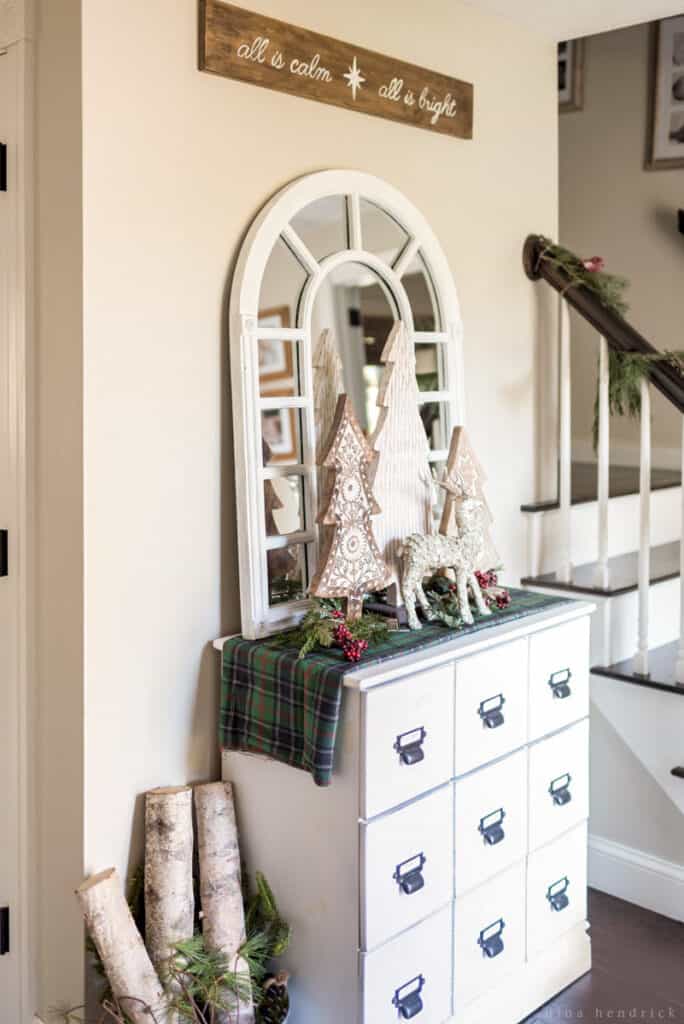 Foyer with white card catalog adorned with a Christmas vignette and an arrangement of birch logs 