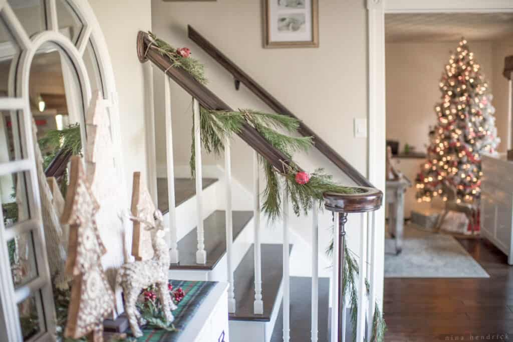 Stair railing decorated with a garland with a Christmas tree sparkling in the background
