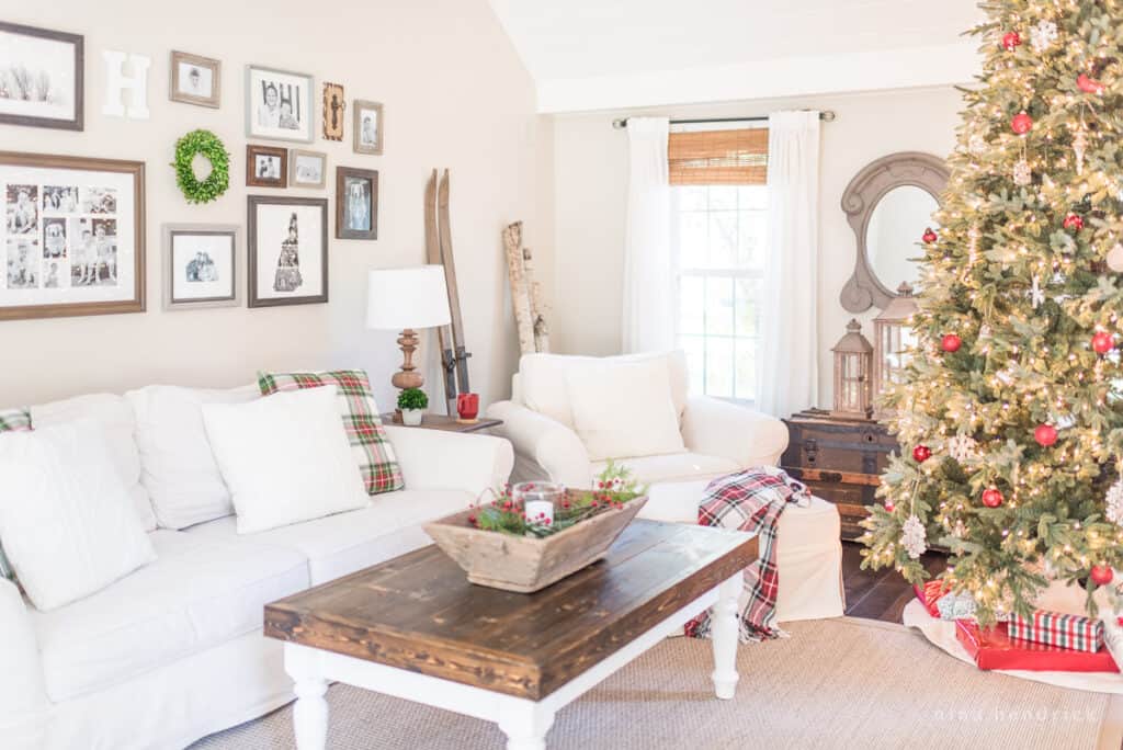 Family room with classic Christmas decorations, white sofas, and a tree decorated with red ornaments