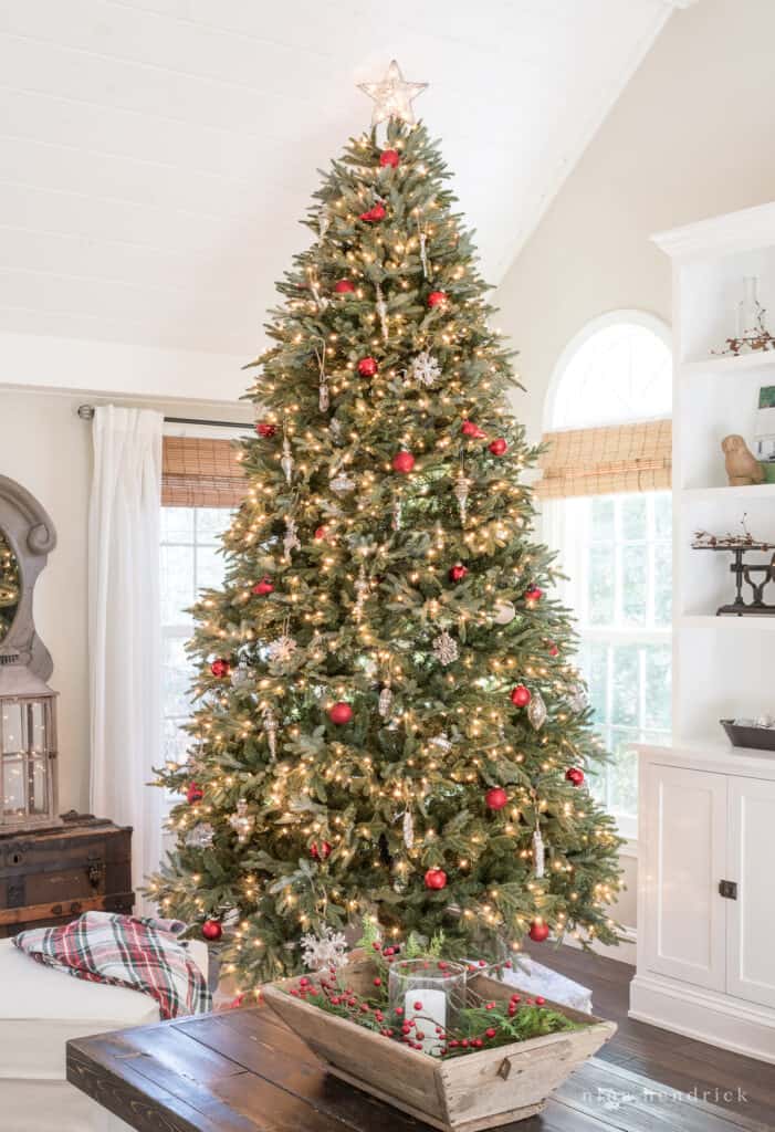 Classic Christmas tree decorations with red ornaments and mercury glass along with a wooden trug centerpiece with a glass hurricane, white candle, and greenery