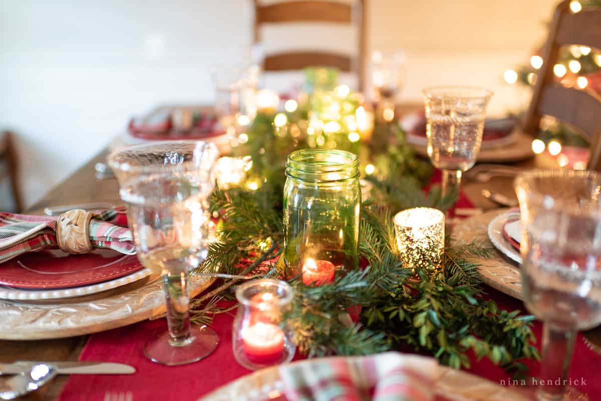 Gather inspiration for your holiday entertaining with this Classic Christmas Tablescape featuring traditional reds and greens. Table with candlelight and green mason jars