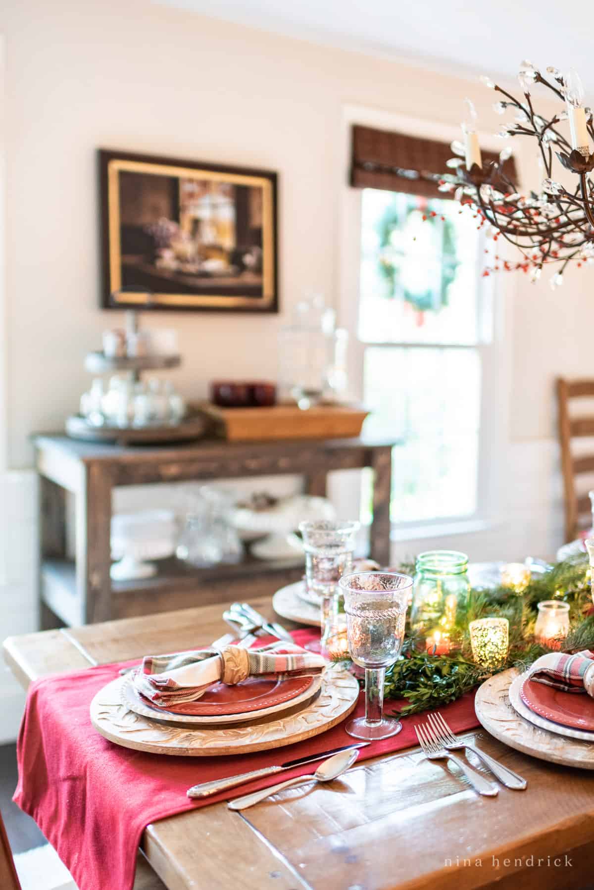 Gather inspiration for your holiday entertaining with this Classic Christmas Tablescape featuring traditional reds and greens. Rustic Christmas table setting with a brown wood cart in the background