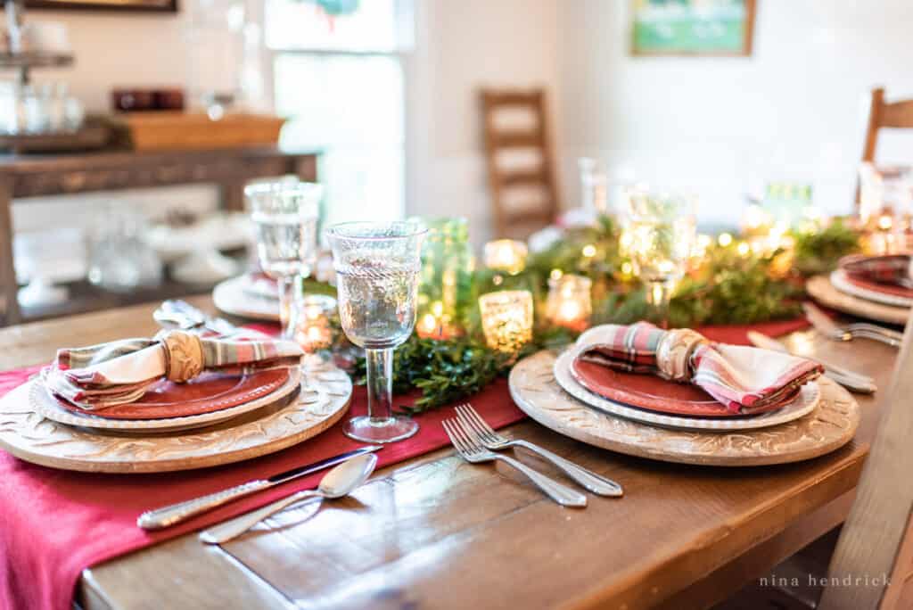 Gather inspiration for your holiday entertaining with this Classic Christmas Tablescape featuring traditional reds and greens. Dishes and place settings with glassware on top of a rustic wood table