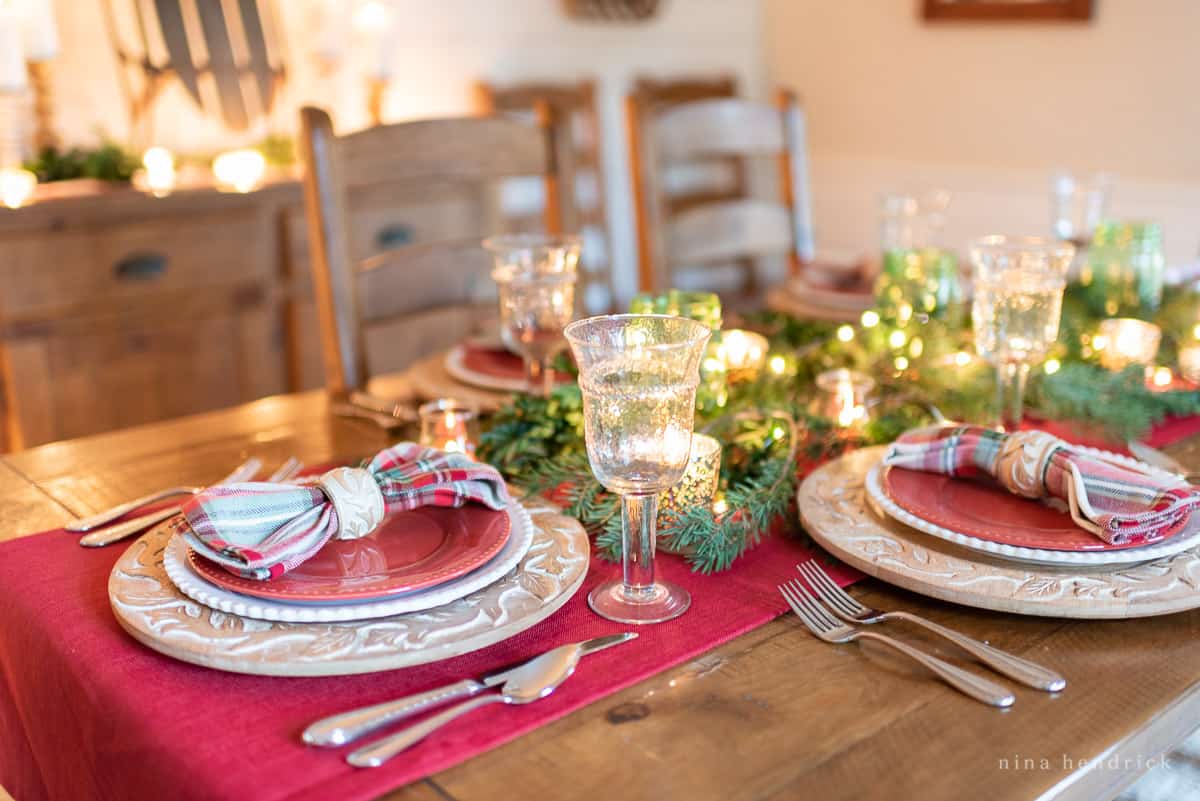 Tabletop with red runner, glassware, and greenery