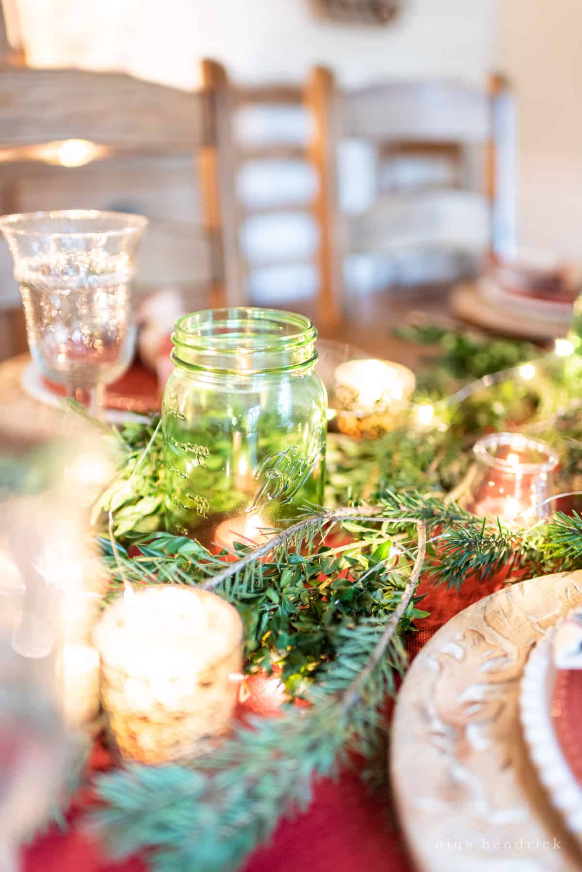 Green mason jar in evergreen centerpiece with holiday twinkle lights and candles