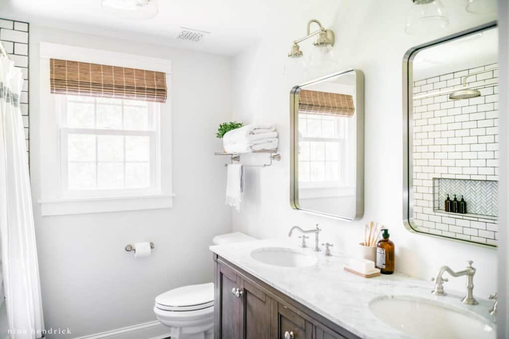 Bathroom with metal-rimmed brushed nickel mirrors and marble countertops.