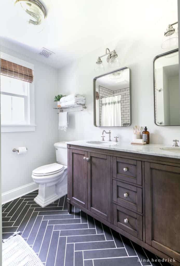 Small bathroom makeover with a dark wood vanity and herringbone tile floor. 