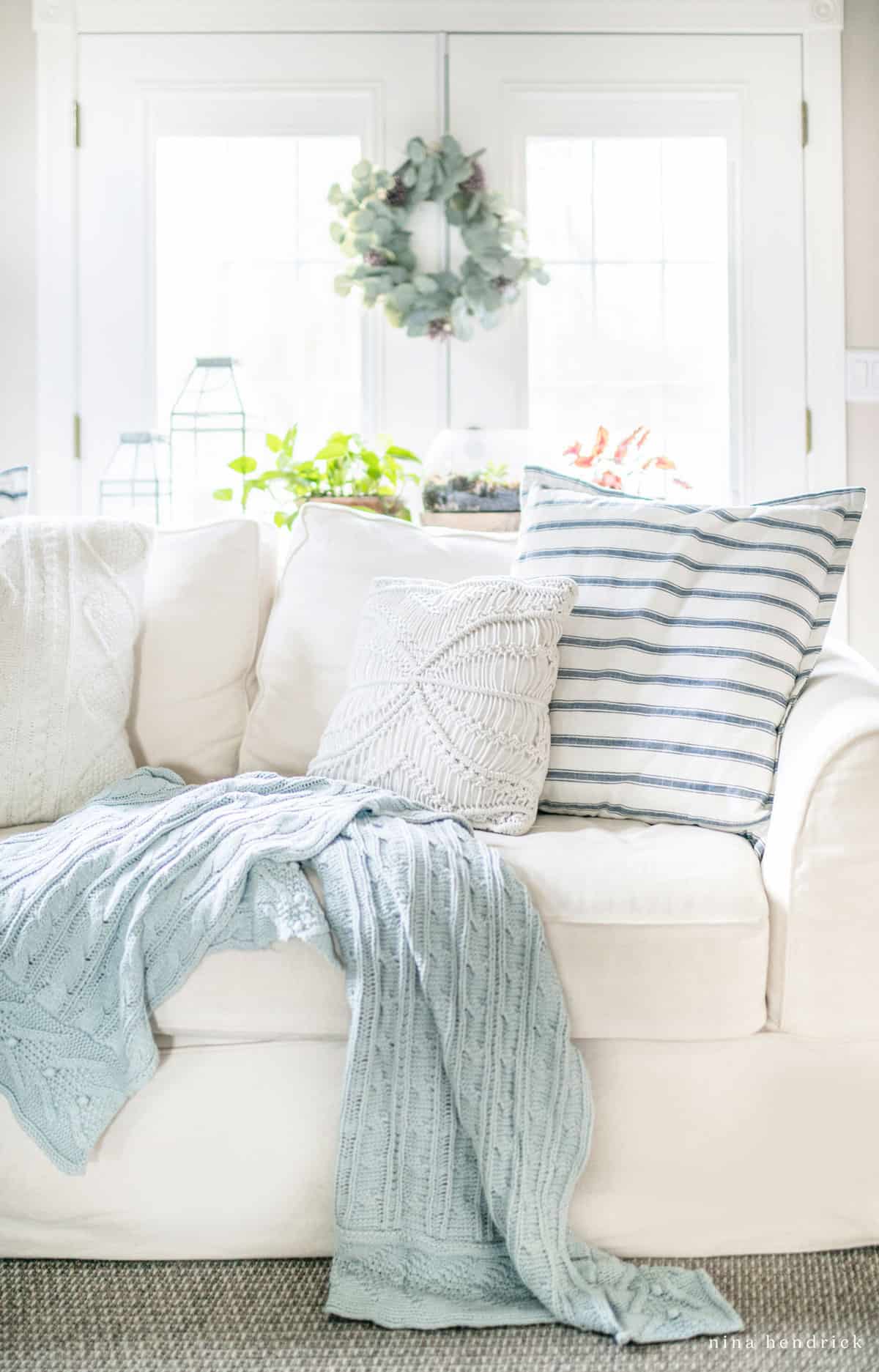 Clean, white slipcovered sofa with white throw pillows and blue accents.