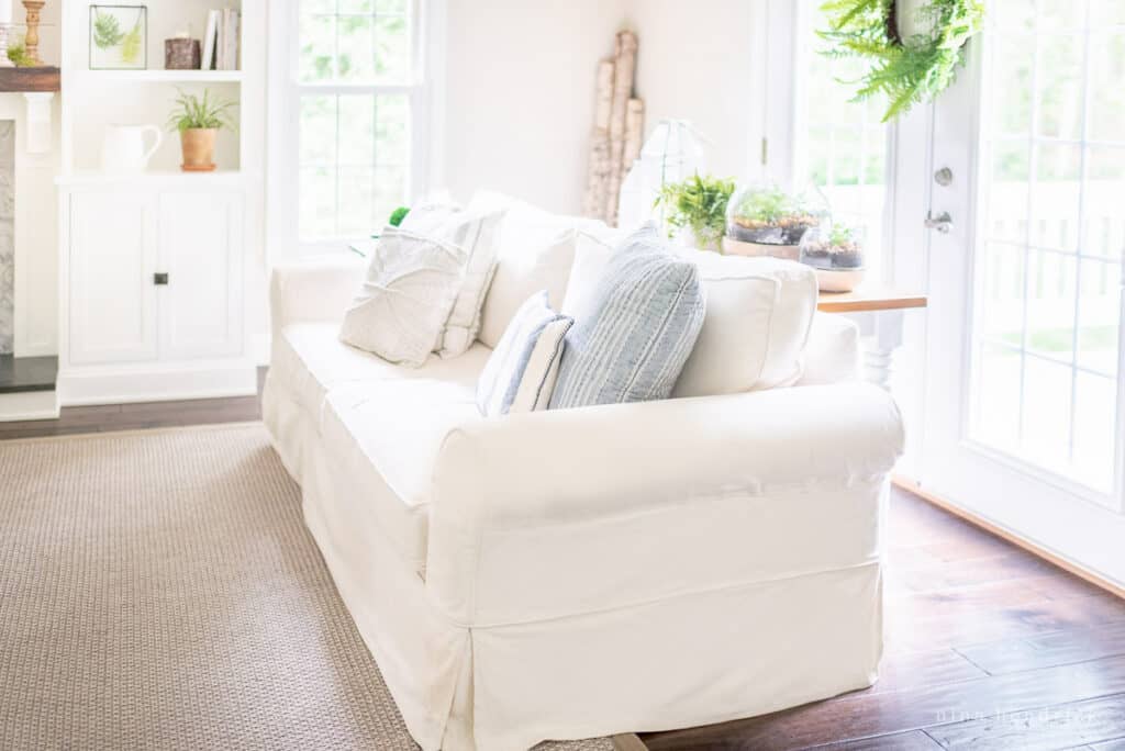 White slipcovered sofa in a family room with blue pillows and greenery