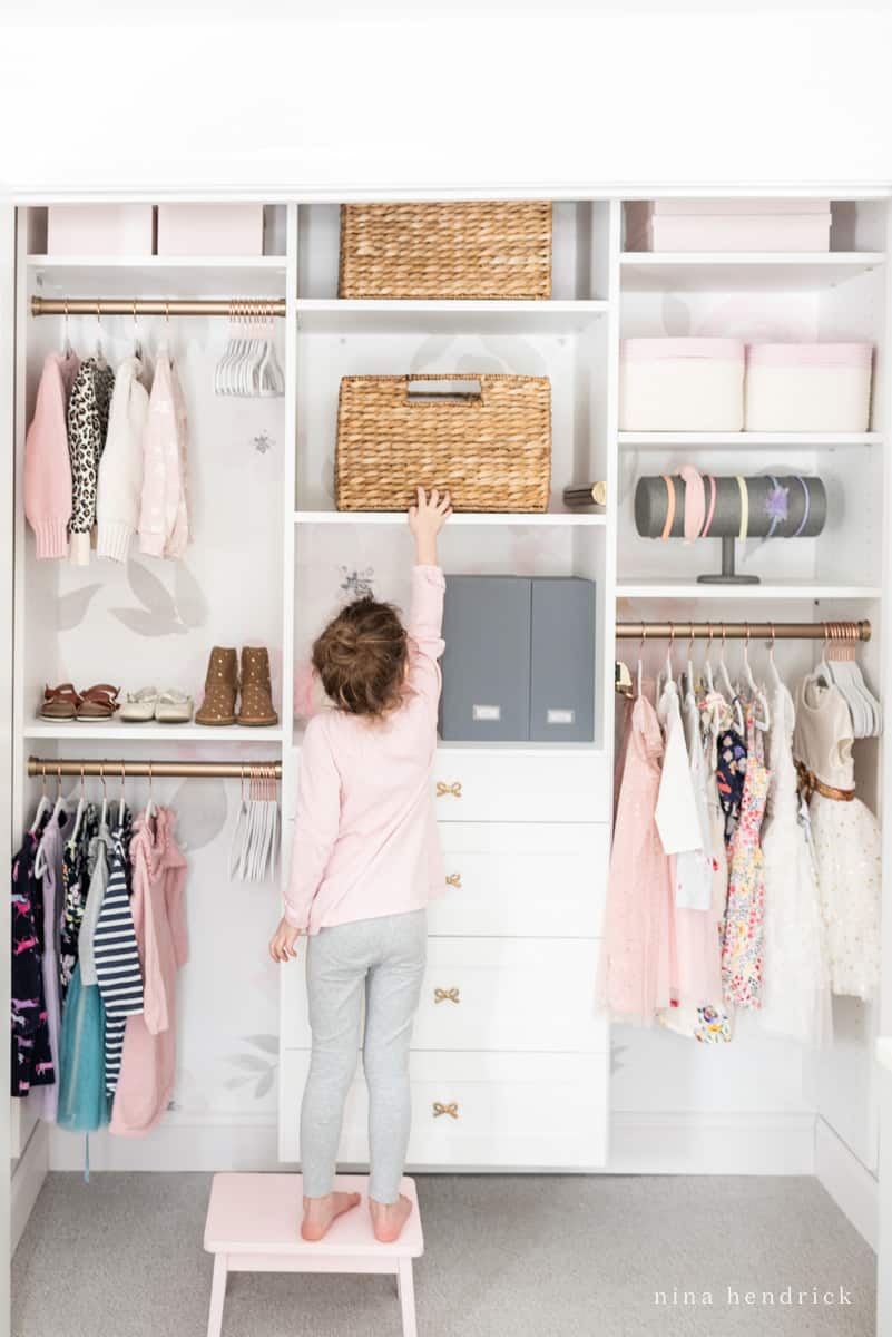 Little girl's organized closet with wicker baskets and floral wallpaper