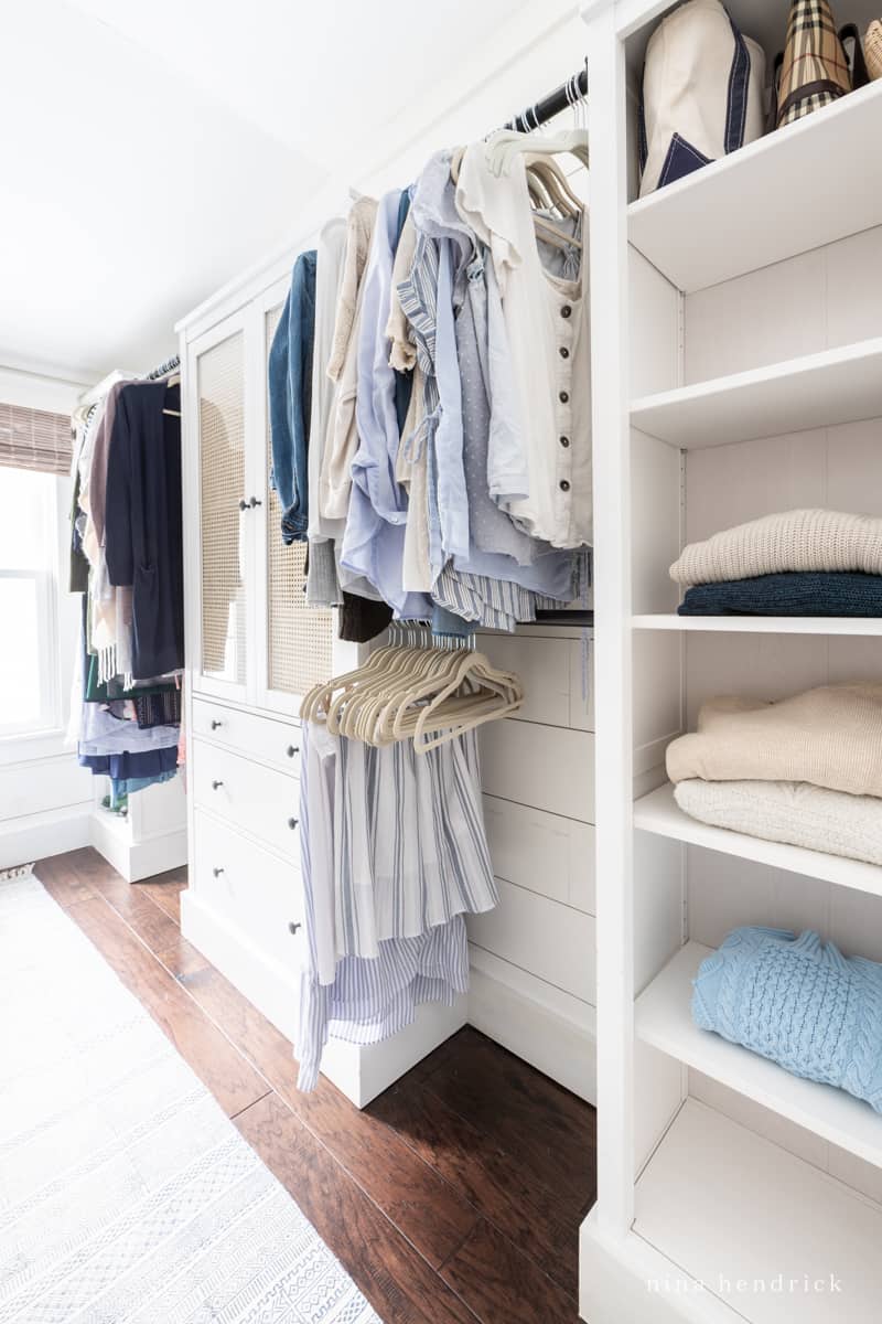 White walk-in clothes storage room with folded blue and tan sweaters