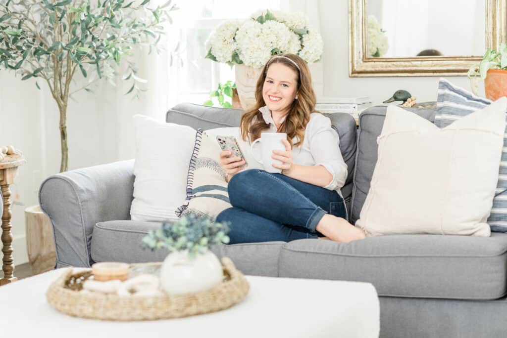 Nina Hendrick in a cozy living room on a blue sofa with throw pillows and hydrangeas showing the coastal grandmother style and trend