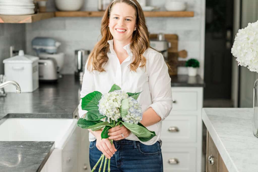 Nina Hendrick in kitchen with white button-down and holding hydrangeas showing the "Coastal Grandmother" aesthetic