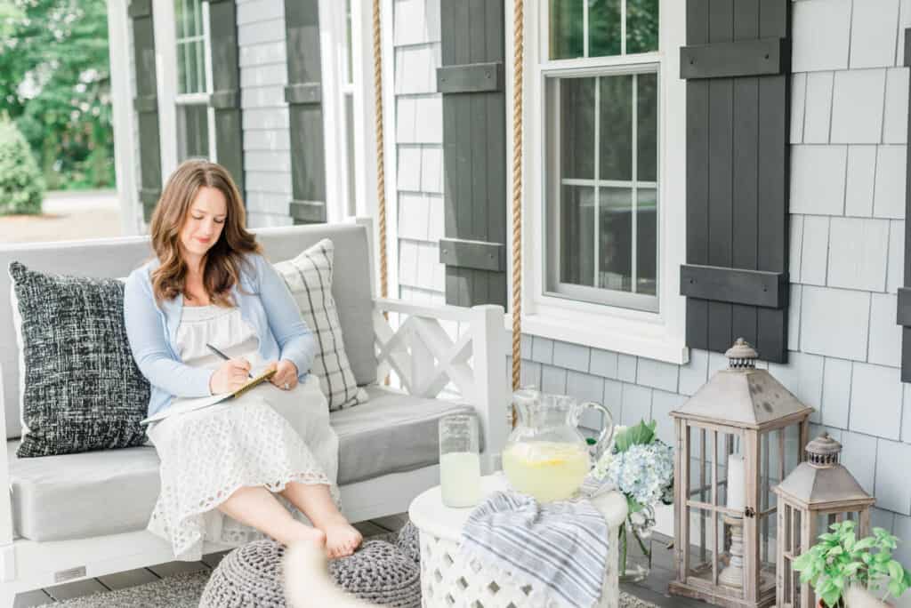 Nina Hendrick sitting on a porch swing on a white swing with blue cardigan capturing the Coastal Grandmother style