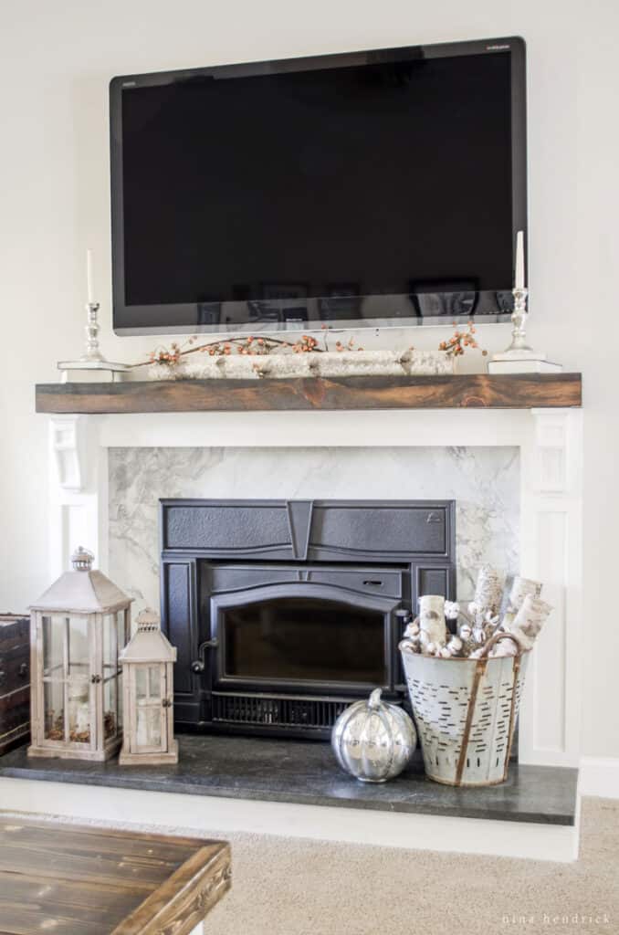 White fireplace with rustic decor and a black TV above