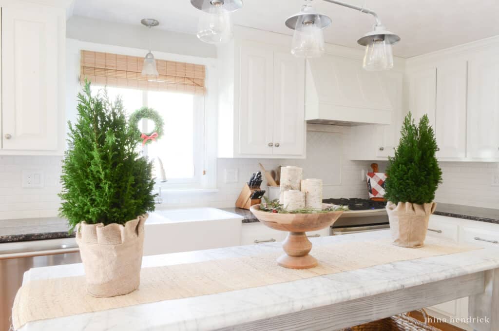 Kitchen with cozy Christmas decorating ideas: rosemary topiaries and a birch candle arrangement on the marble island.