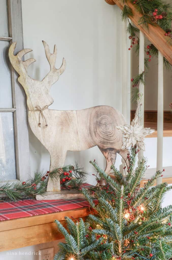 Cozy foyer vignette with wooden deer statue decor and a small Christmas tree lit with twinkle lights.