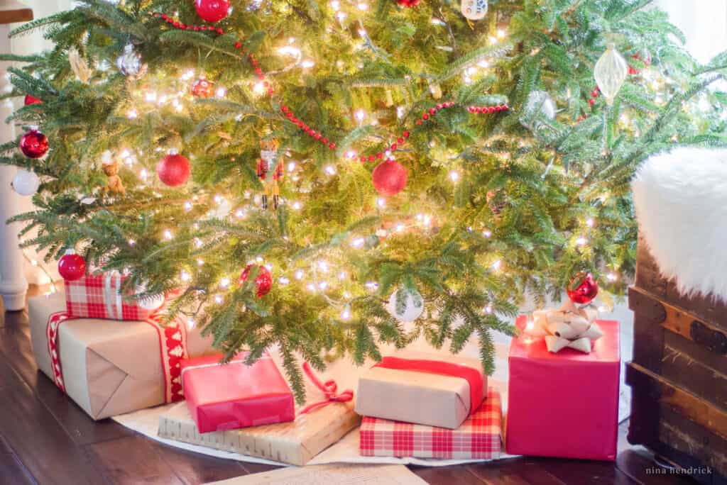 Red and burlap wrapped presents under the natural Christmas tree with ornaments and twinkle lights.