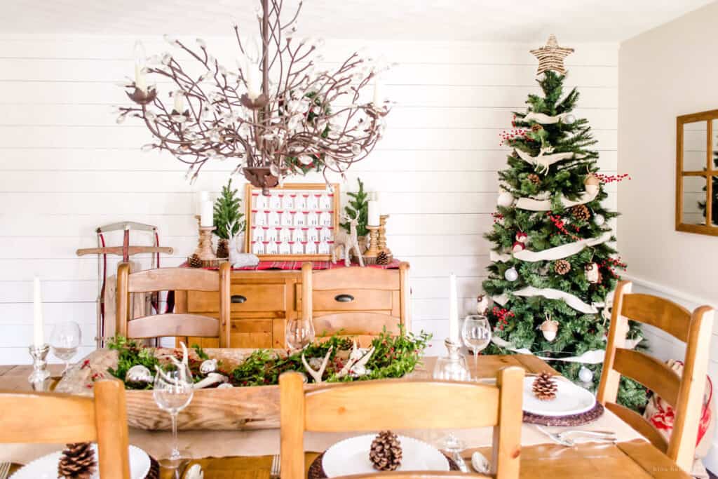 Dining room decorated for a cozy Christmas with white walls and pops of red on a small Christmas tree. 