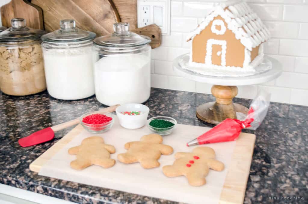 gingerbread men and house with cookie decorating supplies on a granite countertop 