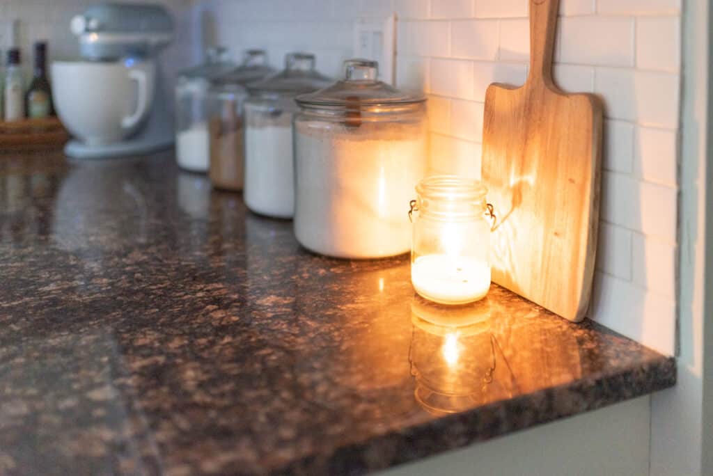 Candle burning on the kitchen counter near jars of dry goods