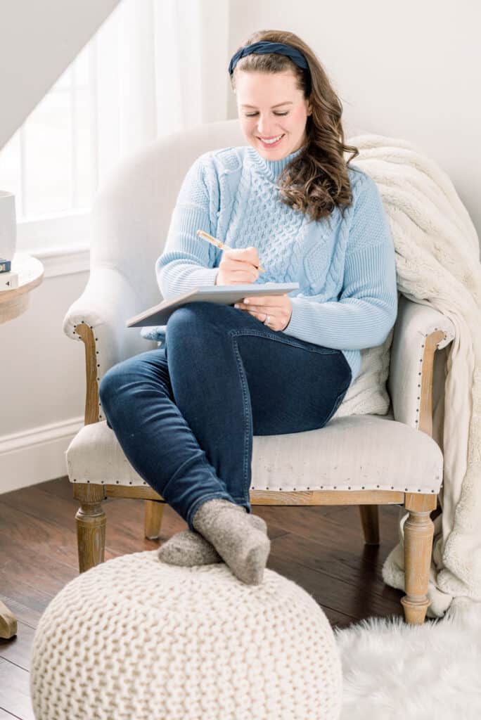 Woman sitting and writing in a cozy chair with faux fur blanket and knitted ottoman