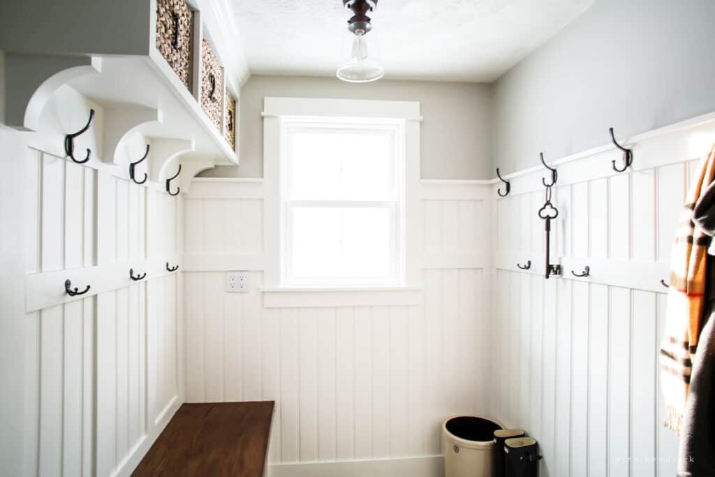 A bright white beadboard mudroom with a sunny window after tranformation of a cramped laundry closet. 