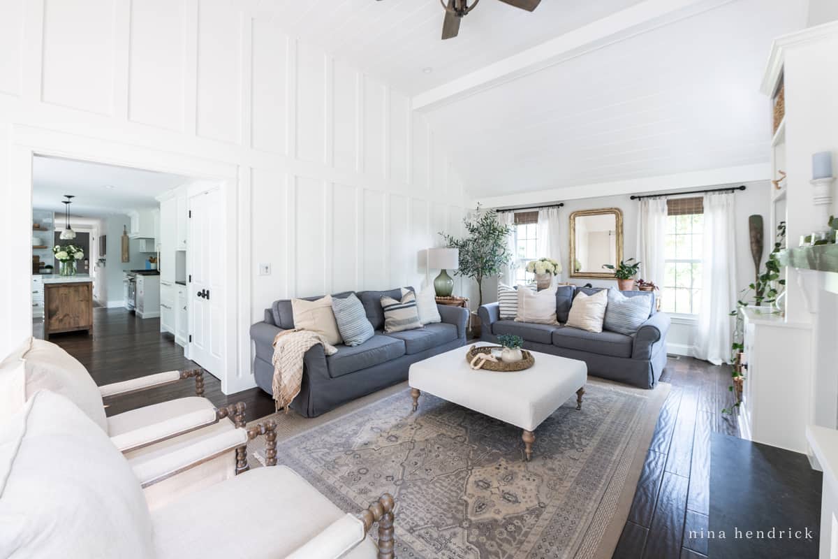 Living room with white board-and-batten wall treatment and a peek into the adjoining kitchen.